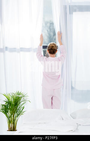 Ansicht der Rückseite Frau im Pyjama öffnen Vorhänge in Morgen Stockfoto