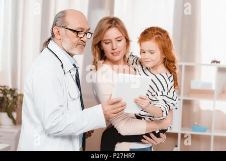 Portrait von Arzt im weißen Kittel, Frau und Tochter mit Tablet zusammen in der Klinik Stockfoto