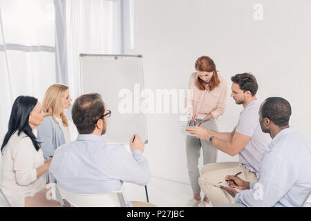 Psychotherapeutin in der Nähe von Tafel und im Gespräch mit Multiethnischen Menschen während der Gruppe Therapie Stockfoto