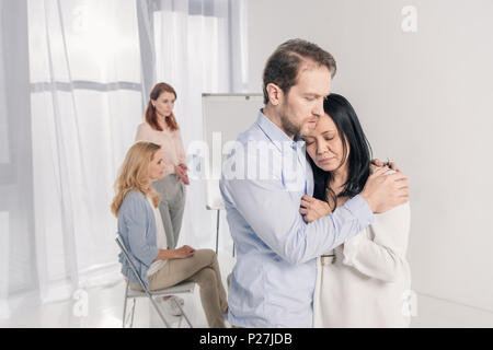 Reifer Mann umarmen gedrückt asiatische Frau während der Gruppe Therapie Stockfoto