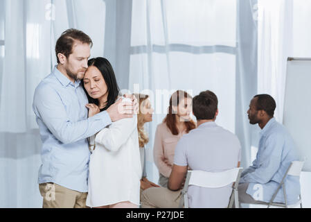 Verärgert reifes Paar umarmt, während die Leute sitzen auf Stühlen hinter während der Gruppe Therapie Stockfoto