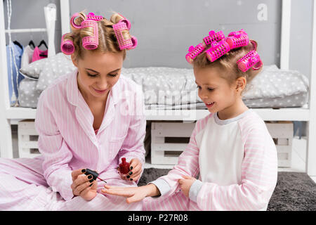 Mutter Malerei Nägel der Tochter mit polnischen, während Sie sitzen im Schlafanzug mit Haar Rollen Stockfoto