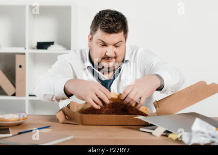 Fat Geschäftsmann essen Pizza zum Mittagessen am Arbeitsplatz Stockfoto