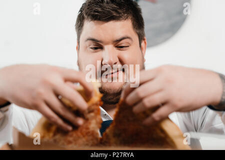 Selektiver Fokus von Übergewicht Geschäftsmann essen Pizza zum Mittagessen am Arbeitsplatz Stockfoto