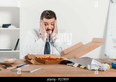 Übergewicht überrascht Geschäftsmann mit Pizza am Arbeitsplatz Stockfoto