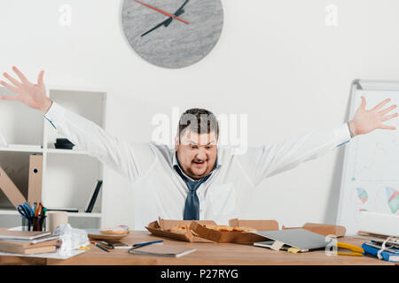 Übergewicht aufgeregt Geschäftsmann mit Pizza am Arbeitsplatz im Büro Stockfoto