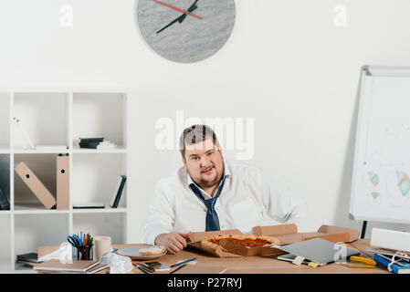 Übergewicht Geschäftsmann essen Pizza am Arbeitsplatz im Büro Stockfoto