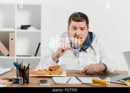 Übergewicht Geschäftsmann Essen der Trödelnahrung am Arbeitsplatz Stockfoto