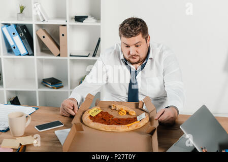 Übergewicht Geschäftsmann bei Pizza, während im Büro sitzen Stockfoto
