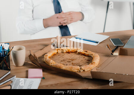 7/8-Ansicht von Fett Geschäftsmann essen Pizza am Arbeitsplatz Stockfoto