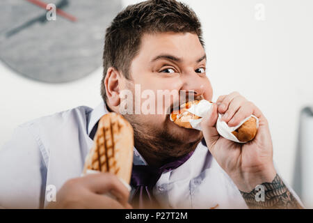 Fat Geschäftsmann essen Hotdogs am Arbeitsplatz im Büro Stockfoto