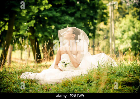 Schöne junge Braut sitzen auf einem Green Glade in einem wunderschönen Wald Stockfoto