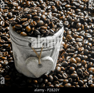 Kaffeebohnen in einem Ton pocoffee Bohnen in einem kleinen Tontopf mit einem Herz auf dem Hintergrund von Kaffee beanst Stockfoto