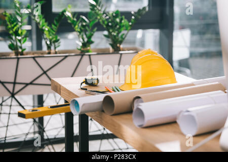 Hardhat, Maßband und Blueprints auf Tisch in der modernen Architekten Büro Stockfoto