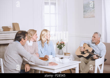 Eleder Mann Gitarre spielen, während ein anderer Leute am Tisch sitzen Stockfoto