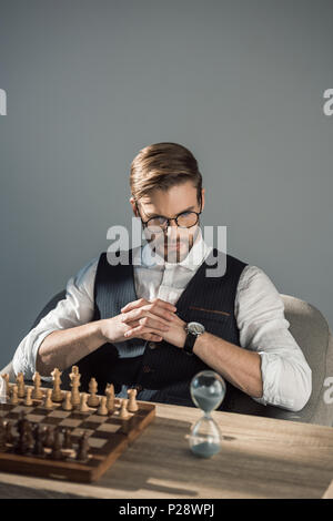 Konzentrierte junge Unternehmer im Sand clock, während Schach spielen Stockfoto