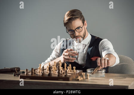 Junge Unternehmer mit einem Glas Whisky und Zigarre Schach spielen Stockfoto