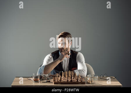 Stilvolle junge Unternehmer mit Zigarre weg schauen beim spielen Schach Stockfoto
