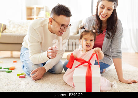 Baby Mädchen mit Geburtstagsgeschenk und Eltern zu Hause Stockfoto