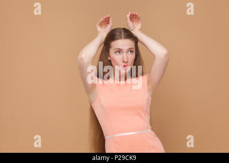 Funny Girl mit Bunny style Hände. Portrait von emotionalen Cute, schöne Frau mit Make-up und langes Haar in rosa Kleid. Indoor, studio Shot, isoliert Stockfoto