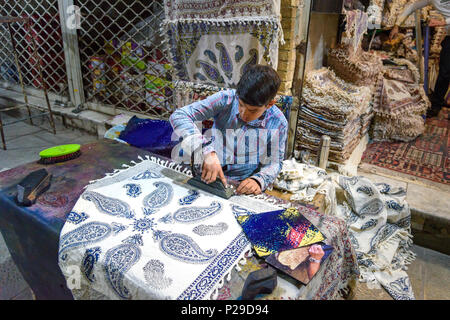 Isfahan, Iran - 21. März 2018: Iranische Junge mit geschnitzten hölzernen Block traditionelle Motive auf Textilien in Grand Bazaar zu Stempeln Stockfoto