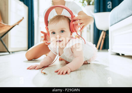 Cute Baby auf dem Boden sitzend zu Hause spielen mit Kopfhörer Stockfoto