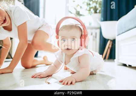 Cute Baby auf dem Boden sitzend zu Hause spielen mit Kopfhörer Stockfoto