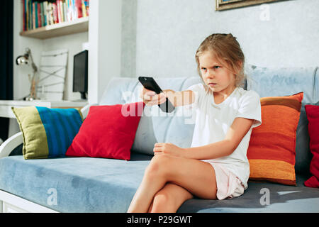 Wenig Casual Mädchen Fernsehen zu Hause. Weibliche Kind sitzt auf einem Sofa mit Fernbedienung und Schaltkanäle Stockfoto