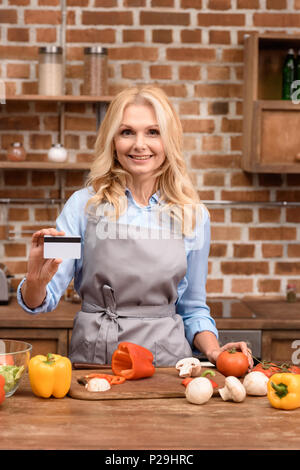 Frau mit Kreditkarte und stehen in der Tabelle mit Gemüse in der Küche Stockfoto