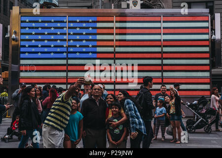 Touristen, die in selfies aus auf einem grossen LED-amerikanische Flagge in Times Square, New, USA. New York ist eine der meist besuchten Städte in der Welt. Stockfoto