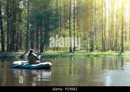 Ein Fischer in einem Boot auf dem Fluss wirft einen Angel Stockfoto