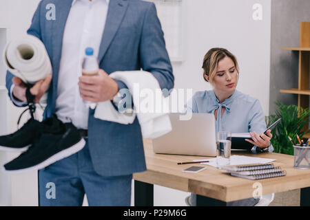 Screenshot des Kaufmanns holding Fitnessgeräte, während seine Kollegen an ihrem Arbeitsplatz 7/8 Stockfoto