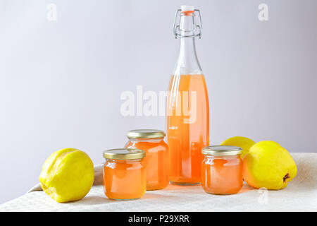 Hausgemachte Quitten Gelee und Saft in Flaschen und Gläsern mit Quitten auf Leinen Tischdecke vor neutralem Hintergrund, kopieren. Stockfoto