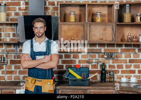 Stattliche junge professionelle Handwerker mit Werkzeug Gürtel stand mit verschränkten Armen und Kamera Stockfoto