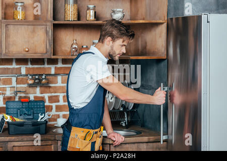 Seitenansicht des hübscher junger Handwerker zur Festsetzung Kühlschrank Stockfoto