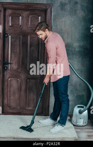 Junger Mann mit Staubsauger und Reinigung Teppich zu Hause Stockfoto