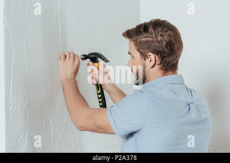 Junger Mann hämmern Nagel in der Wand zu Hause Stockfoto