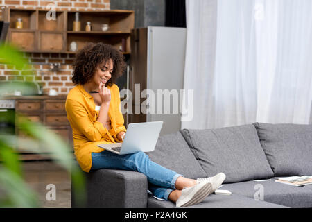 Attraktive junge Frau mit Laptop zu Hause arbeiten mit unscharfen loft Küche auf Hintergrund Stockfoto