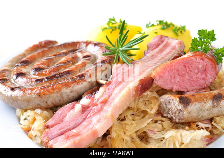 Bauch von Schweinefleisch und verschiedenen Würstchen auf Sauerkraut mit gekochten Kartoffeln, weißer Hintergrund Stockfoto
