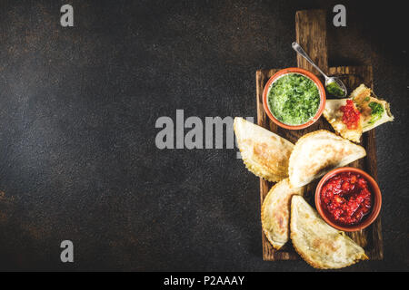 Latein amerikanischen, mexikanischen, chilenischen Essen. Traditionelle gebackenes Gebäck Empanadas mit Rindfleisch, zwei würzige Saucen, dunklen rusty Background Copy space Stockfoto