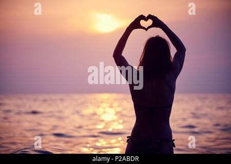 Herzform mit Händen gemacht, das Morgen die Sonne am Horizont. Herz gegen schönen Sonnenuntergang. Stockfoto