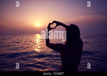 Herzform mit Händen gemacht, das Morgen die Sonne am Horizont. Herz gegen schönen Sonnenuntergang. Stockfoto