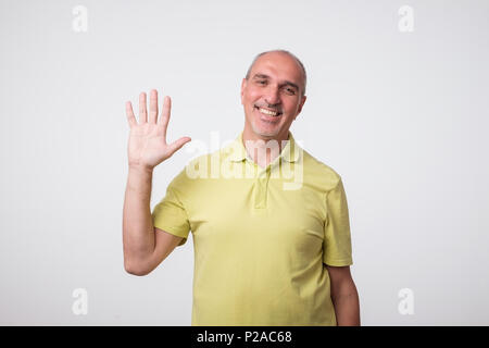 Freundlich - auf der Suche attraktiven europäischen Mann verzichtet auf Hand in hallo Geste während fröhlich lächelnd. Host ist froh, seine Gäste oder Freunde herzlich Willkommen Stockfoto