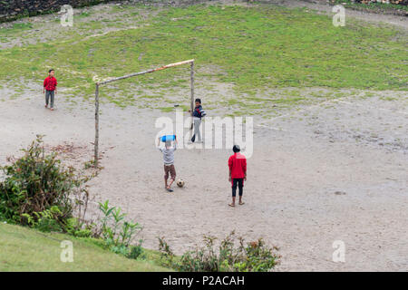 GHALEGAUN, Nepal - ca. Mai 2018: Kinder spielen Fußball, einer von ihnen tragen eine blaue Becken auf seinem Kopf. Das Ziel ist der Baum verzweigt. Stockfoto