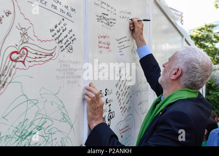 London, Großbritannien. 14. Juni 2018. Jeremy Corbyn, der Führer, schreibt eine Nachricht auf die Mauer der Erinnerung an der Basis der Grenfell Tower. Tribute gibt es in der Umgebung die 72 Leute, die auf dem Jahrestag der Tragödie Grenfell Turm, wo eine kleine Küche Feuer in die größte Blaze in Großbritannien gesehen seit dem Zweiten Welt Krieg getötet wurden, zu erinnern. Viele Menschen tragen grüne Schals - Grün für Grenfell - in Erinnerung an diese verloren. Credit: Stephen Chung/Alamy leben Nachrichten Stockfoto