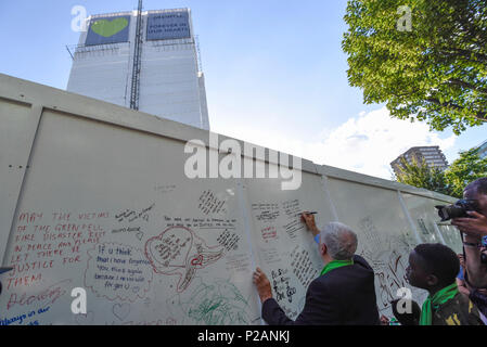 London, Großbritannien. 14. Juni 2018. Jeremy Corbyn, der Führer, schreibt eine Nachricht auf die Mauer der Erinnerung an der Basis der Grenfell Tower. Tribute gibt es in der Umgebung die 72 Leute, die auf dem Jahrestag der Tragödie Grenfell Turm, wo eine kleine Küche Feuer in die größte Blaze in Großbritannien gesehen seit dem Zweiten Welt Krieg getötet wurden, zu erinnern. Viele Menschen tragen grüne Schals - Grün für Grenfell - in Erinnerung an diese verloren. Credit: Stephen Chung/Alamy leben Nachrichten Stockfoto