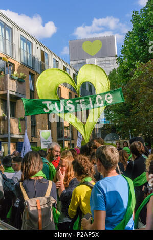 London, Großbritannien. 14. Juni 2018. Grenfell Tower, jetzt überdacht und mit einem Herzen auf seine Oberseite Webstühle über Menschen, die sich in der Stille aus der Nähe von Grenfell Turm der Erinnerung an die Opfer der Katastrophe am ersten Jahrestag der Brandkatastrophe, die getötet 72 und linke Überlebende traumatisiert zu gehen. Viele von denen, die ihr Obdach verloren haben durch das Feuer noch in Befristete Unterkunft ein Jahr später trotz der Versprechungen mde von Theresa und Kensington und Chelsea, der viele fielen die lokale Gemeinschaft sowohl vor als auch nach dem Brand versagt haben. Sie sagen, wurden sie zugehört und Grenfell respektiert würden nicht Stockfoto