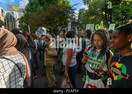 London, Großbritannien. 14. Juni 2018. Grenfell Tower, jetzt überdacht und mit einem Herzen auf seine Oberseite Webstühle über Menschen, die sich in der Stille aus der Nähe von Grenfell Turm der Erinnerung an die Opfer der Katastrophe am ersten Jahrestag der Brandkatastrophe, die getötet 72 und linke Überlebende traumatisiert zu gehen. Viele von denen, die ihr Obdach verloren haben durch das Feuer noch in Befristete Unterkunft ein Jahr später trotz der Versprechungen mde von Theresa und Kensington und Chelsea, der viele fielen die lokale Gemeinschaft sowohl vor als auch nach dem Brand versagt haben. Sie sagen, wurden sie zugehört und Grenfell respektiert würden nicht Stockfoto