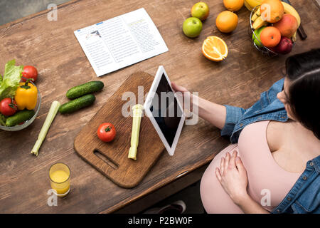 7/8 Schuß von jungen schwangeren Frau mit digitalen Tablet beim Kochen in der Küche Stockfoto