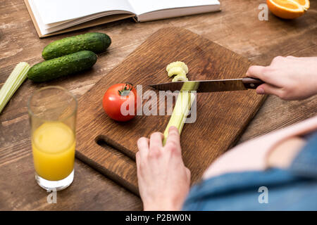 7/8 Schuß von Frau schneiden Sellerie auf Holz Schneidebrett Stockfoto